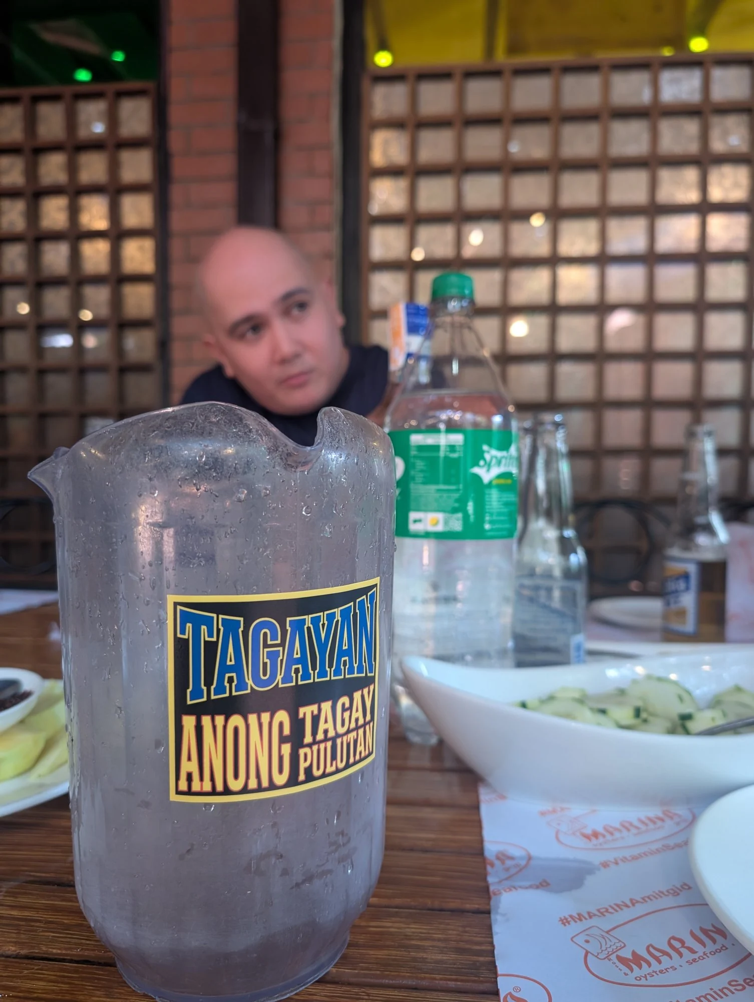 A TAGAYAN pitcher on a restaurant table with bottles and a bowl of sliced cucumber behind it.