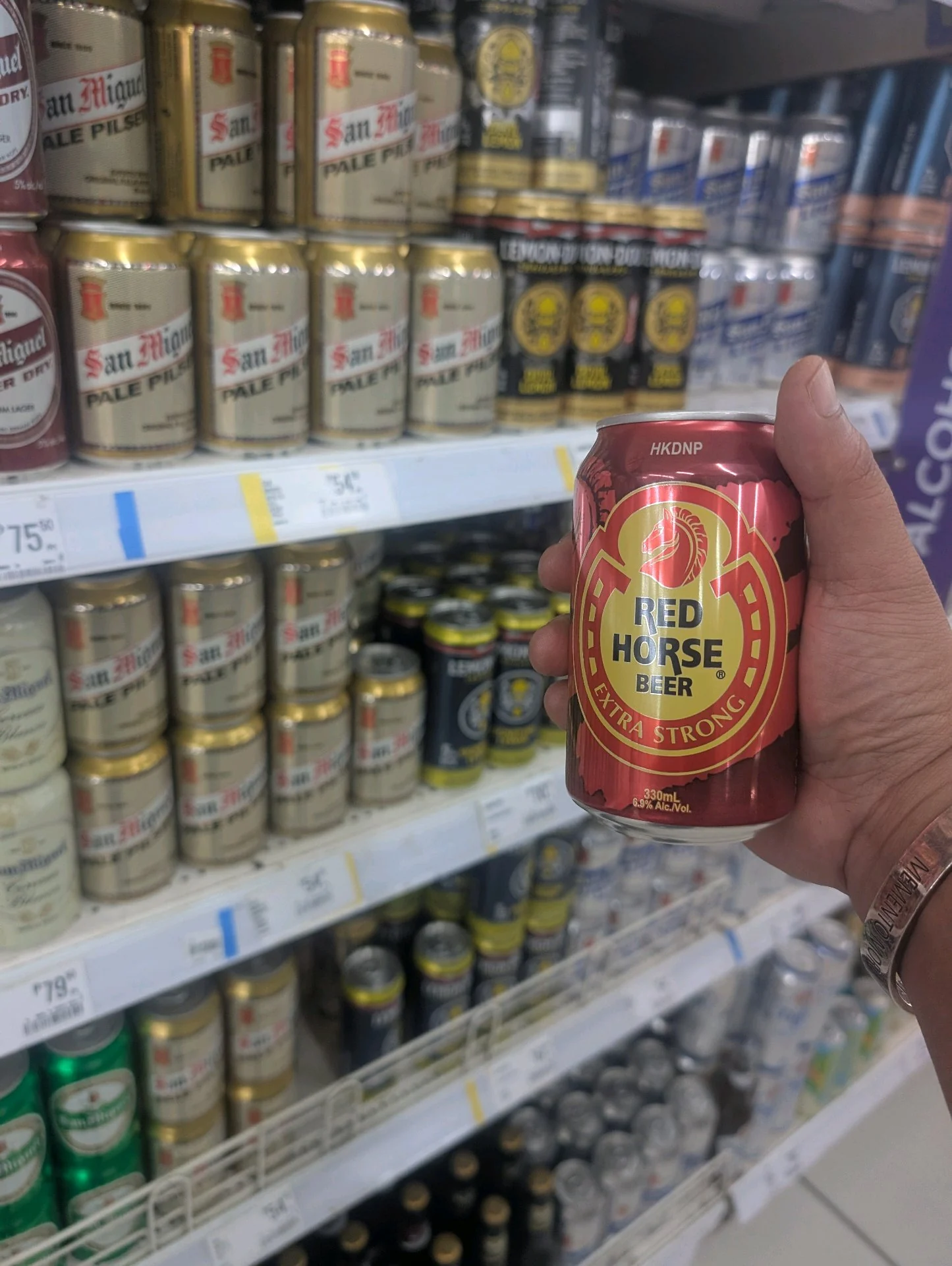 A hand holding a 330 mL can of Red Horse Beer marked Extra Strong, 6.9% alc./vol., in front of a store shelf.